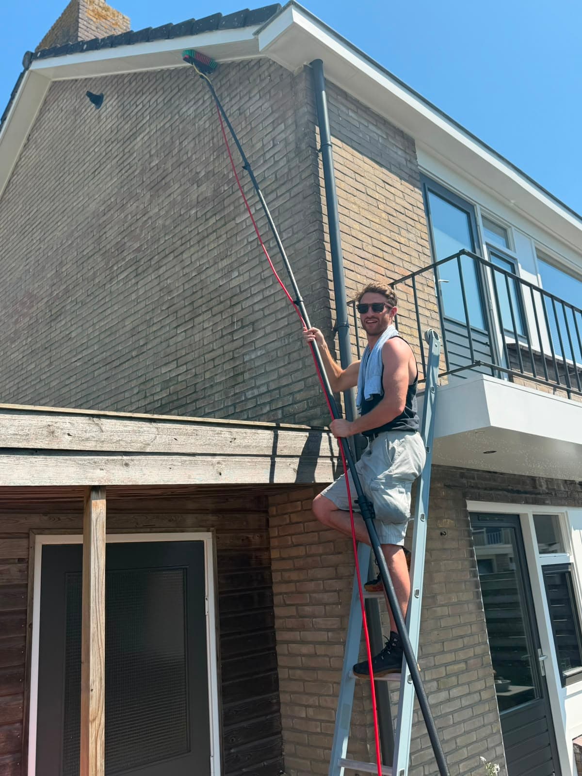 Glazenwasser van Madern werkt vanaf een ladder met een watergevoede telescoopsteel aan de dakrand van een woning in Apeldoorn
